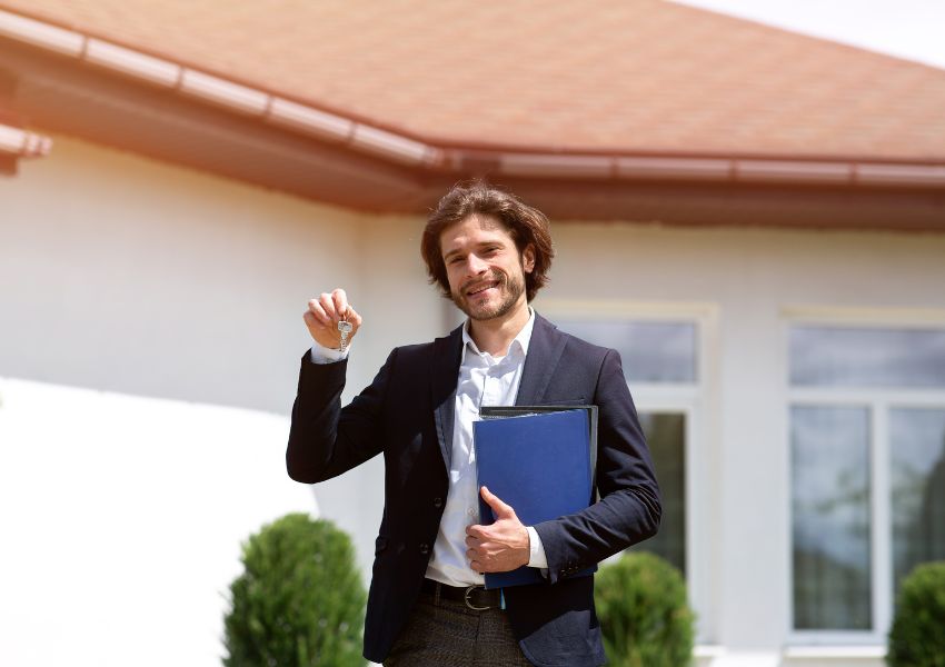 A property manager in a suit holds a blue folder and keys outside a rental unit.